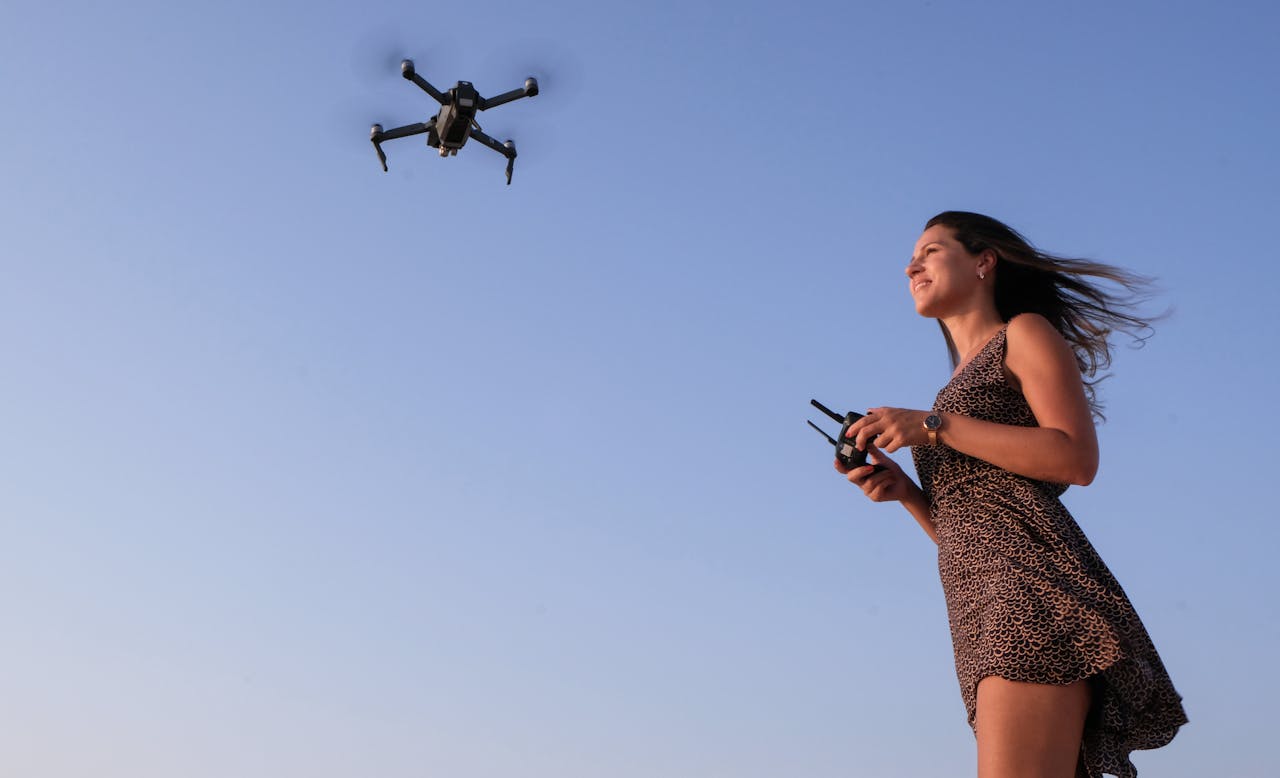 services-04 A woman enjoying flying a drone outdoors under a clear blue sky.