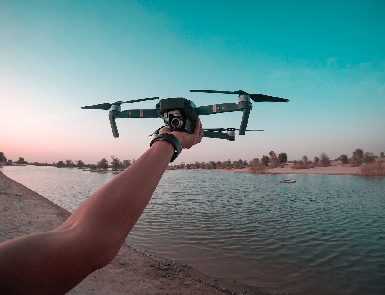 gallery-01 A person holds a drone over a lake in the Dubai desert, showcasing a scenic aerial view.