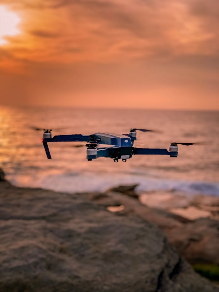 services-img A drone hovers over a rocky shoreline with a stunning sunset backdrop, creating a serene atmosphere.
