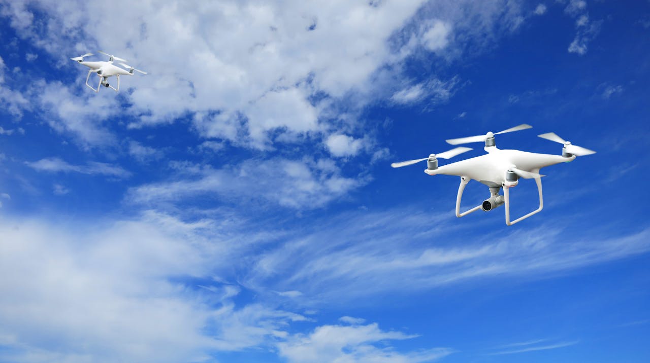 A stunning capture of two drones flying against a bright blue sky with soft clouds.