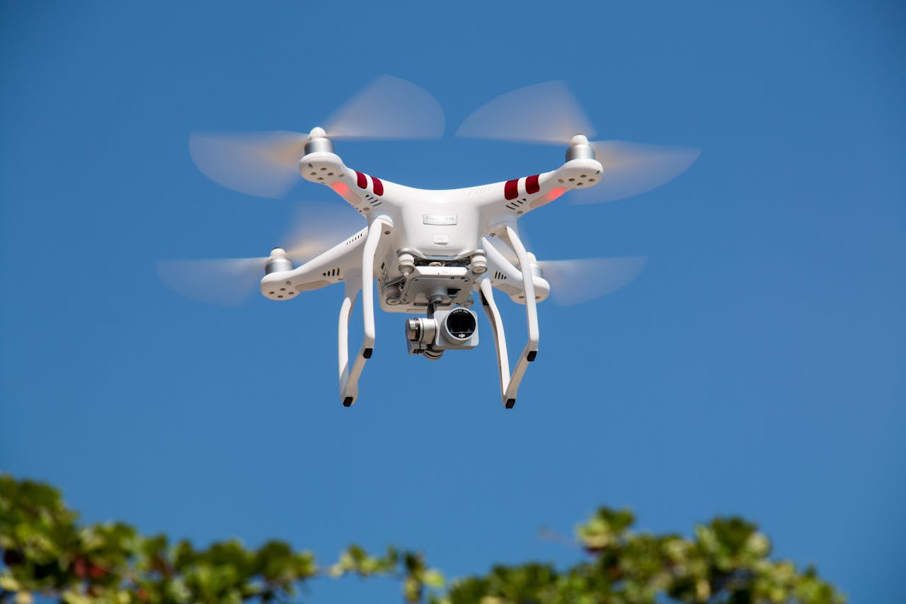 about-img-01 A white drone flying with camera against a clear blue sky in La Libertad.