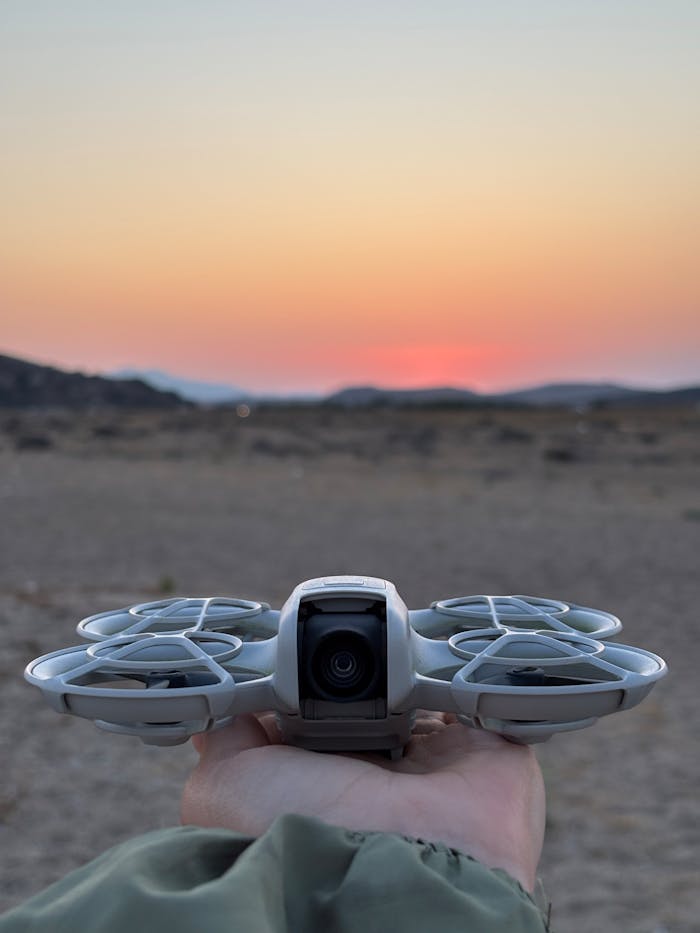 about-img Silhouette of a drone held against a vivid sunset in a desert landscape.