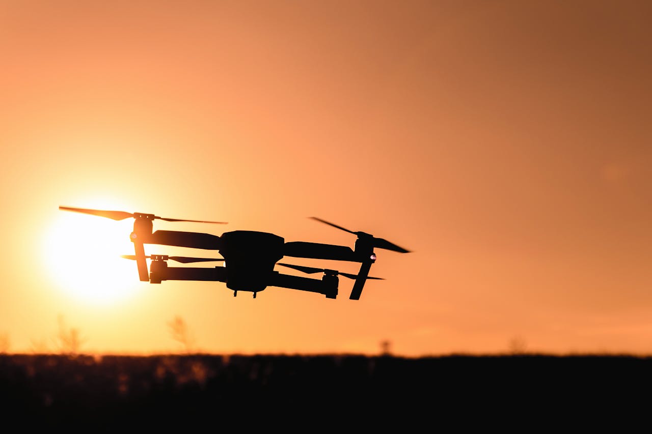 gallery-05 A drone in silhouette against a vibrant orange sunset sky, showcasing modern technology and aerial photography.